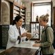 Pharmacist in a white coat explaining a medicine to a young woman at the counter of a traditional pharmacy in Seville