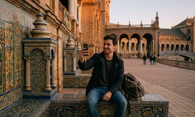 Young man video-calling his family on a smartphone while sitting on a tiled bench in Seville's Plaza de España at dusk