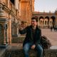 Young man video-calling his family on a smartphone while sitting on a tiled bench in Seville's Plaza de España at dusk