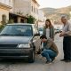 Young couple inspecting a second-hand car with an older seller on a sunny residential street in Málaga province