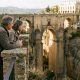 Older couple at a Ronda viewpoint looking at the Puente Nuevo bridge over the El Tajo gorge in late-afternoon light