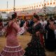 Women in flamenco dresses dancing sevillanas under lanterns at an Andalusian feria