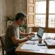Man doing his Spanish tax return on a laptop at a kitchen table with receipts in a sunny apartment