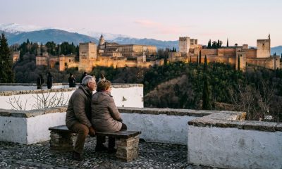 Retired couple on a bench in the Albaicín at dusk looking across to the lit Alhambra and snowy Sierra Nevada