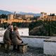 Retired couple on a bench in the Albaicín at dusk looking across to the lit Alhambra and snowy Sierra Nevada