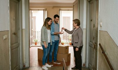 Landlady handing apartment keys to an expat couple in the doorway of a Spanish flat with moving boxes