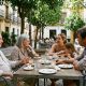 Three generations of a family chatting over coffee after a late lunch on a shaded terrace in a Seville plaza