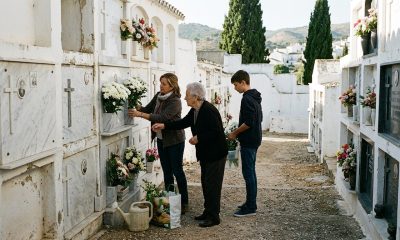Three generations of a Spanish family placing chrysanthemums on a cemetery niche in an Andalusian village on a sunny morning