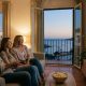 Expat family laughing on the sofa while watching TV through a media box in a Spanish living room with a sea view
