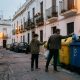 Father and teenage son putting sorted rubbish into colourful recycling containers on a whitewashed street in Cádiz at dusk