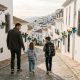 Father walking two young children with school backpacks along a whitewashed street in Mijas on a sunny morning