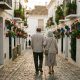 Older couple walking through a whitewashed Estepona street lined with colourful flowerpots at golden hour