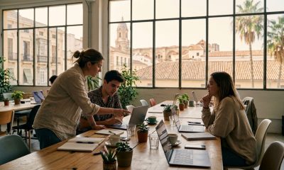 Three young professionals working together in a bright coworking space in Malaga with old town rooftops behind