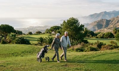 Older couple walking along a golf fairway with sea and mountain views on the Costa del Sol in early morning light