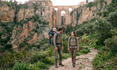 Young couple with a toddler in a carrier hiking below Ronda's Puente Nuevo at sunrise in spring