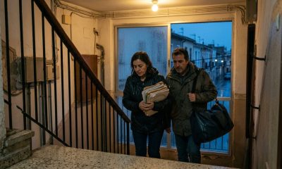 Middle-aged couple carrying a waterproof bag up a stairwell during heavy autumn rain in a Valencian apartment block