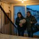 Middle-aged couple carrying a waterproof bag up a stairwell during heavy autumn rain in a Valencian apartment block