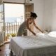 Owner in her forties making a bed with fresh linen in a sunny whitewashed holiday apartment in Nerja