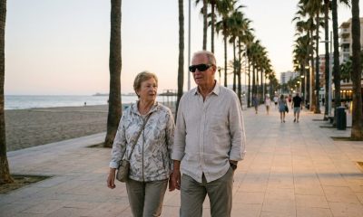 Older expat man in protective sunglasses after eye surgery walking with his wife on a seafront promenade in southern Spain