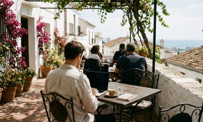 Remote worker with a laptop at a café terrace in a white Andalusian village with bougainvillea and sea view