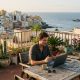 Young man working remotely on a video call from a rooftop terrace in Las Palmas with the ocean behind him