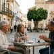 Retired couple in their seventies chatting with a local neighbour at a cafe table in an Andalusian town square at sunset