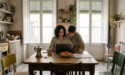 Woman at a kitchen table in Valencia using a laptop and phone to set up her Spanish digital certificate while her son watches