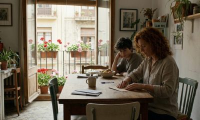 Woman sealing a postal vote envelope at her kitchen table in a sunny Spanish apartment while her son watches