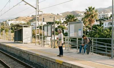 Older woman and teenage boy waiting on a sunny train platform in Benalmádena on the Costa del Sol in the morning