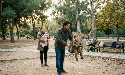 Young father pushing a toddler on a swing while the mother holds a newborn in a park in Valencia