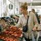 Young mother with a toddler in the trolley choosing tomatoes in a bright supermarket produce aisle in Valencia